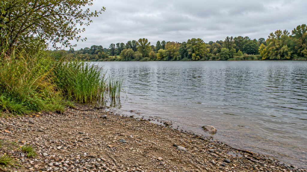 Flaches kiesiges Ufer an einem See mit freier Wasserfläche