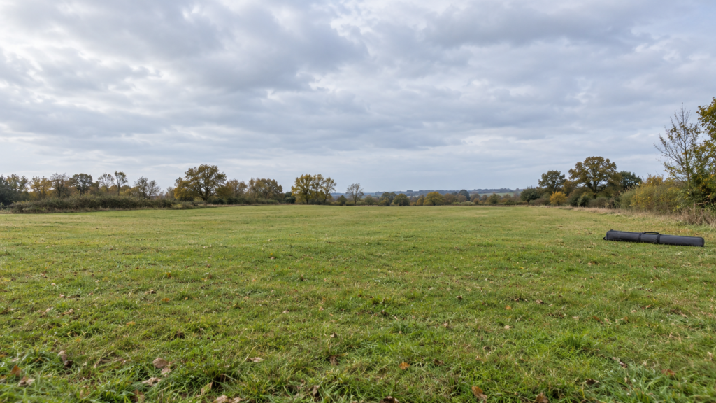 Freie kurzgrasige Wiese mit einem geschlossenen Rutenfutteral am äußeren Rand und offenem Himmel über der Fläche.