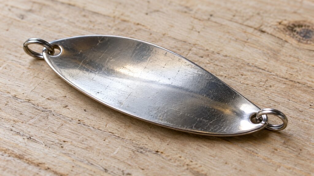 Ein einzelner Metallblinkerkörper mit zwei Sprengringen liegt ohne Haken auf Holz