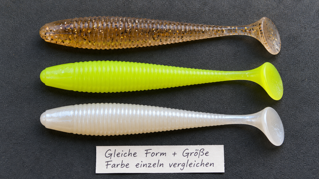 Drei gleich geformte unmontierte Gummishads in Braun, Chartreuse und Weiß auf einer dunklen Unterlage